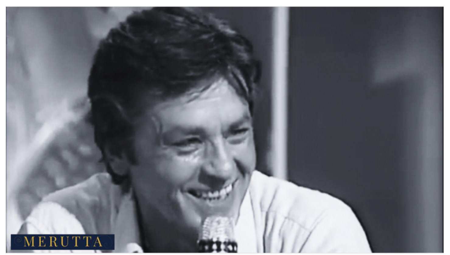 Alain Delon smiling in a classic black and white portrait, French cinema icon.